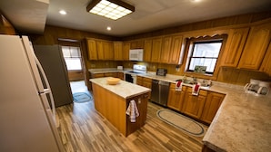 A kitchen with wooden cabinets, a central island, a refrigerator, a microwave, a dishwasher, and a coffee maker.