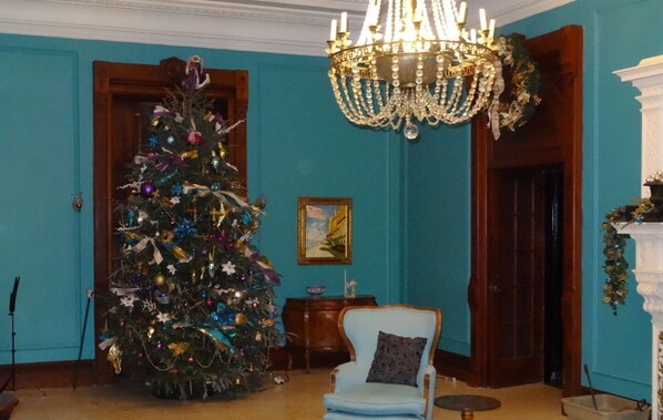 A room with a decorated Christmas tree, a chandelier, and a blue armchair.