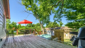 Une terrasse en bois avec un jacuzzi, un parasol rouge et une table avec des chaises.