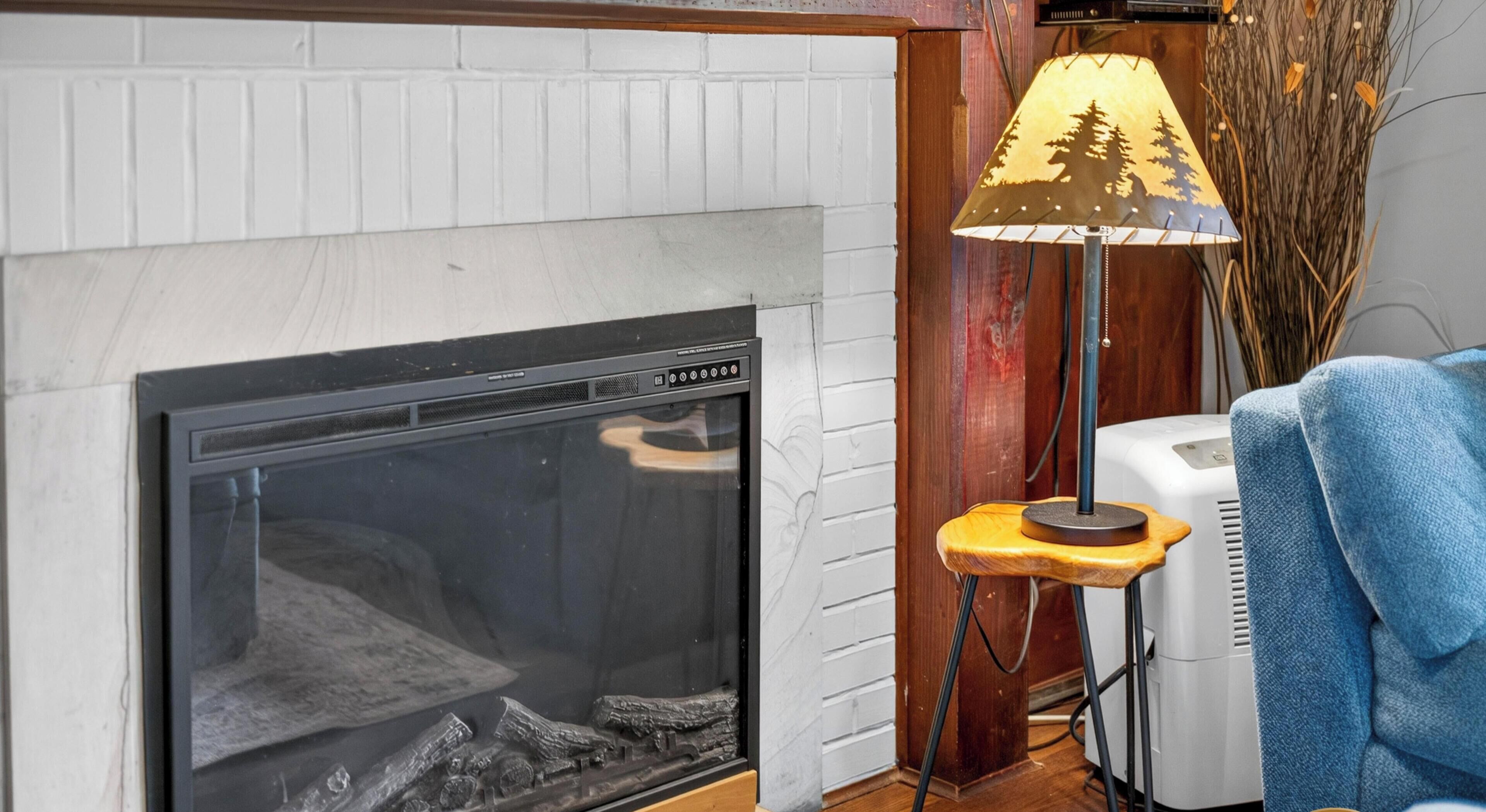Een open haard met een modern ontwerp, een staande lamp met een silhouet van een bos, en een witte radiator.