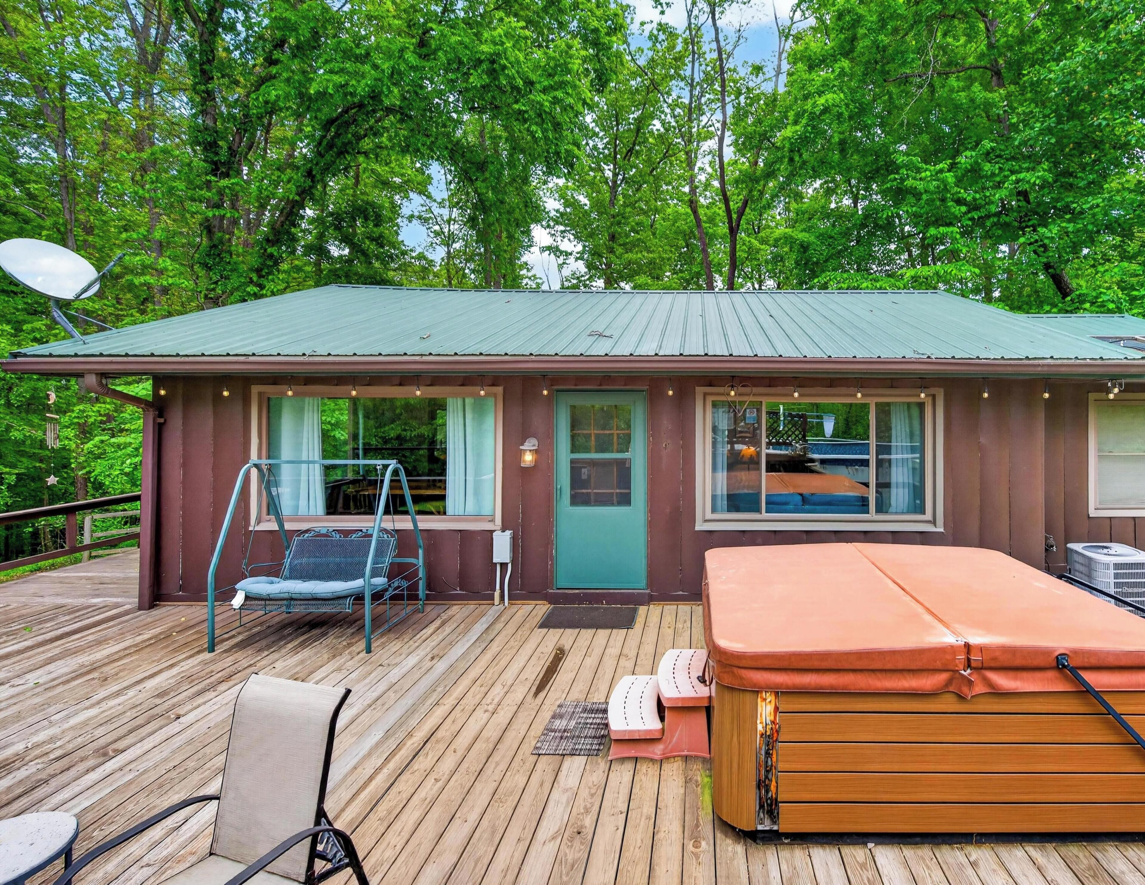 A cabin with a deck, a swing chair, a hot tub, and a satellite dish.