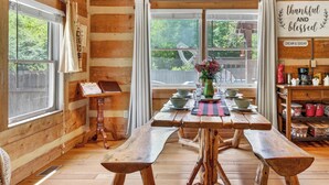 Een rustiek houten interieur met een houten tafel, bankjes, een kroonluchter en uitzicht op groen.