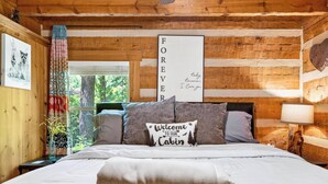 Houten cabin met een bed, kussens, een welkomstbord, een hartvormige decoratie en een ingelijst bericht aan de muur.