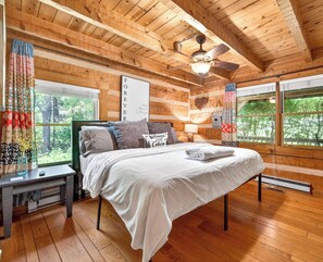 A wooden cabin-style bedroom with a bed, nightstands, a ceiling fan, and large windows. - Log cabin, pets, close to Nashville. (Nashville)