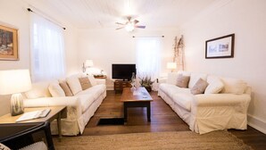 Ein Wohnzimmer mit zwei weißen Sofas, einem Holztisch, einem Fernseher und einem Deckenventilator.