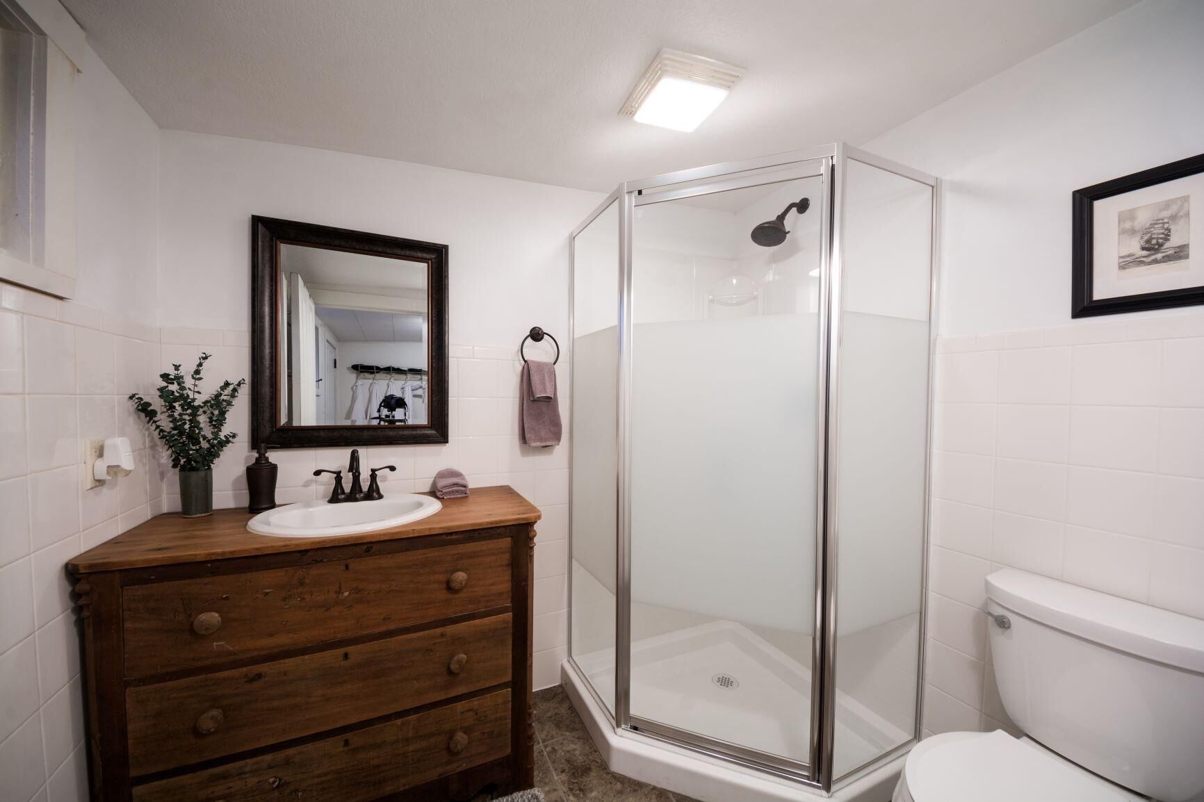 A bathroom with a wooden vanity, a white sink, a mirror, a glass shower enclosure, and a toilet.