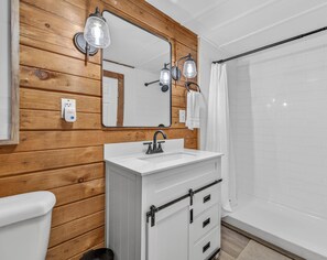 A bathroom with a wooden wall, a white sink, a mirror, and a shower curtain. - Pet friendly, secluded, close to Nashville! (Nashville)