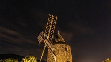 Een stenen windmolen in de nacht met een ladder, omringd door rotsen en bomen.