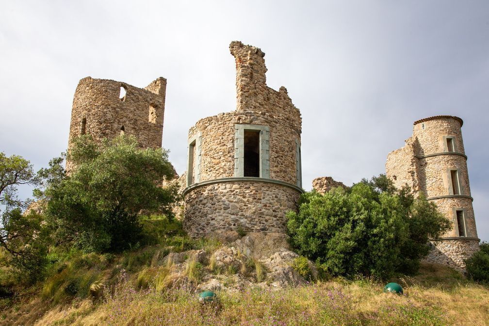 Un’antica struttura in pietra con rovine, tra cui una torre centrale con un’apertura e mura circostanti.