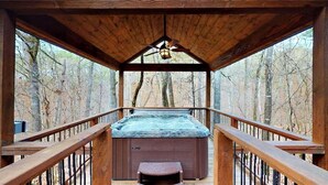 Una cabaña de madera con jacuzzi, barandillas de madera y vista al bosque.