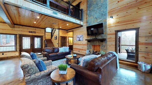 Interior espacioso de una cabaña de madera con sala de estar, chimenea y balcón.