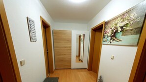 A hallway with wooden flooring, a bench, a mirror, and a painting of flowers.