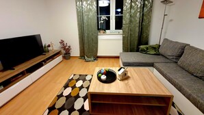 A living room with a sofa, a coffee table, a TV, and a window with curtains.