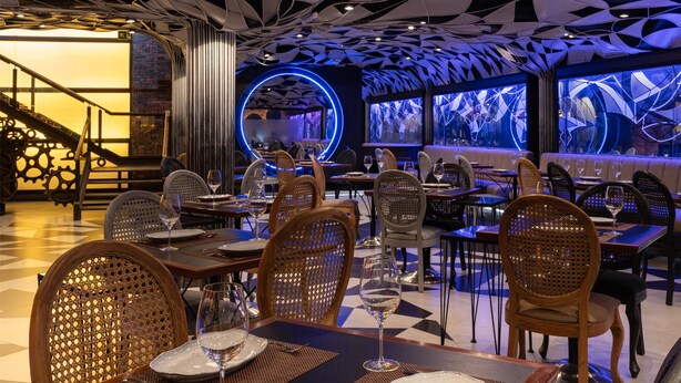 Un restaurant doté d’un plafond au design moderne, de chaises en bois et de tables dressées pour le service.