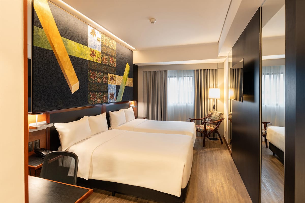 Een hotelkamer met twee bedden, een bureau, een stoel, een bureaulamp en een groot kunstwerk aan de muur.