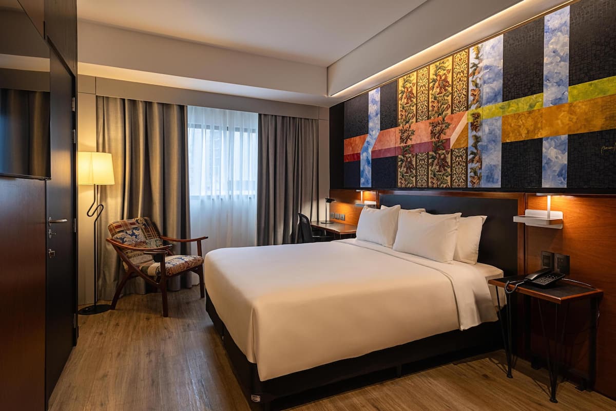 Een hotelkamer met een groot bed, een stoel, een bureau en een kunstwerk aan de muur.