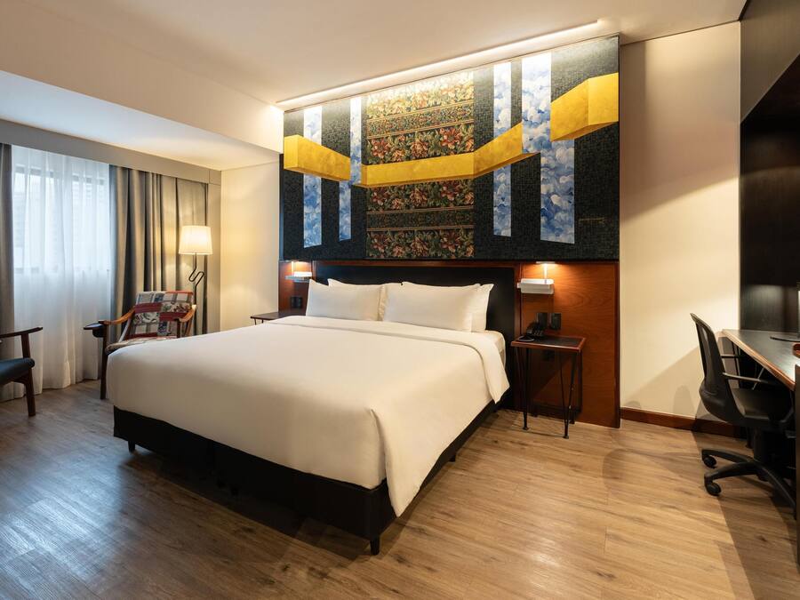 A hotel room with a large bed, a desk, a chair, and a nightstand.