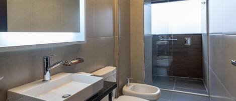 Un baño moderno con un espejo grande, un lavamanos, un bidé y una ducha.