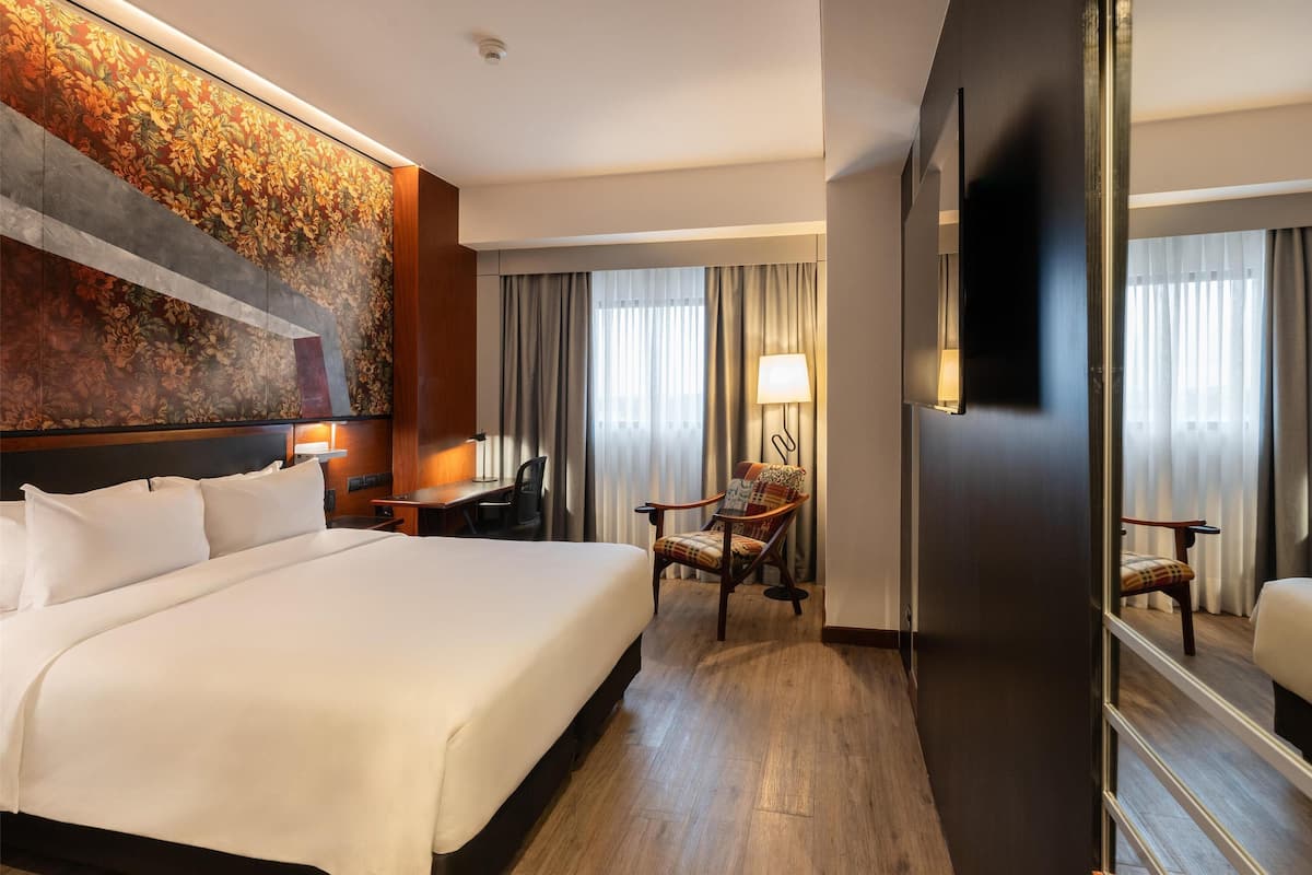 Een hotelkamer met een groot bed, een bureau, een stoel, een televisie en een decoratieve wand.
