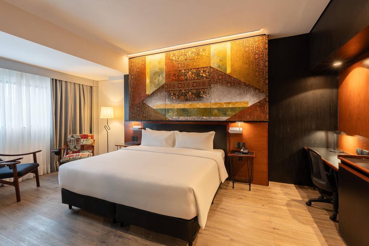 Een hotelkamer met een groot bed, een bureau, een stoel en een decoratief wandobject.