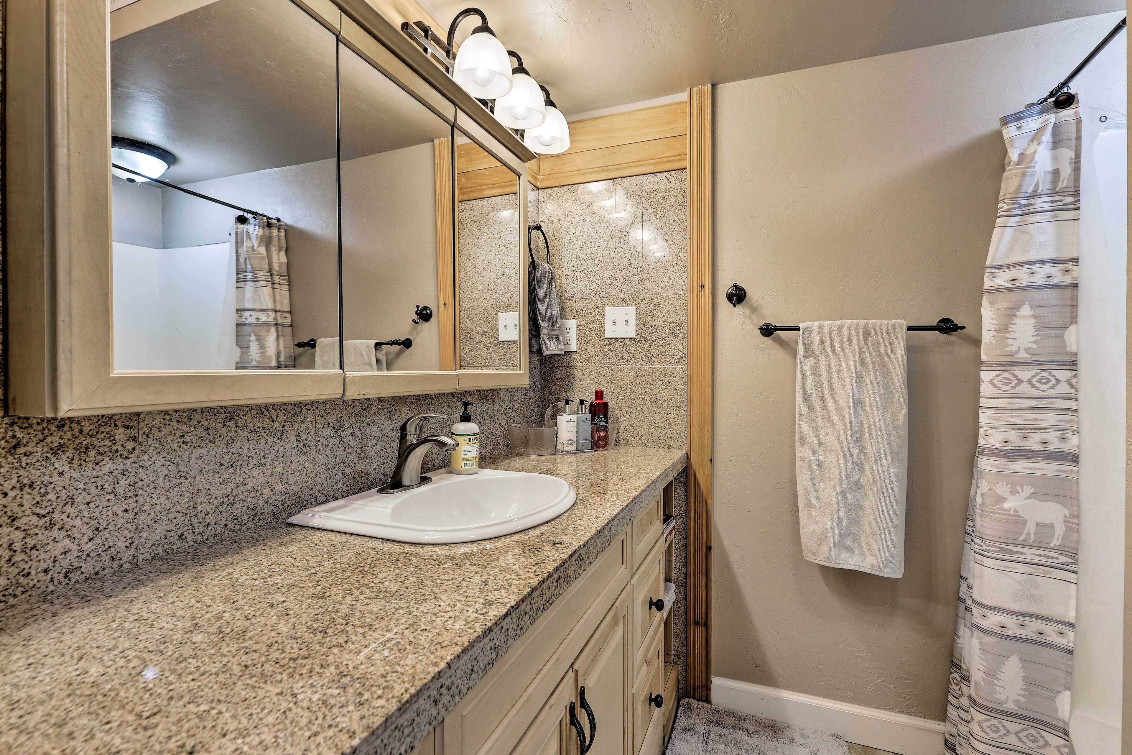 Baño con encimera de granito, lavamanos blanco, espejo con iluminación, toallero y cortina de ducha con estampado de alce.