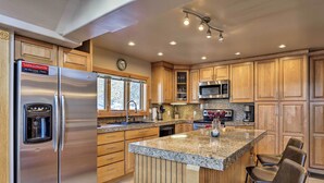 A modern kitchen with wooden cabinets, stainless steel appliances, a granite countertop, and bar stools. - Hot Tub Relaxation: Breck Gem 3 Mi to Skiing! (Breckenridge)
