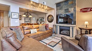 A spacious living room with a leather sofa, a fireplace, and a mounted television. - Hot Tub Relaxation: Breck Gem 3 Mi to Skiing! (Breckenridge)