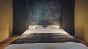 A bedroom with a large bed, wooden headboard, and a textured wall behind the bed. - Meguru House Kyoto (Kyoto)