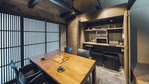 A modern dining area with a wooden table, chairs, and a kitchen in the background. - Meguru House Kyoto (Kyoto)