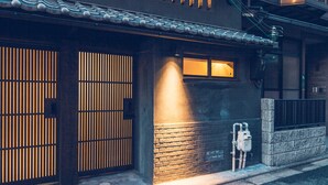 En traditionel japansk bygning med en træport, en lille veranda og en murstensmur.