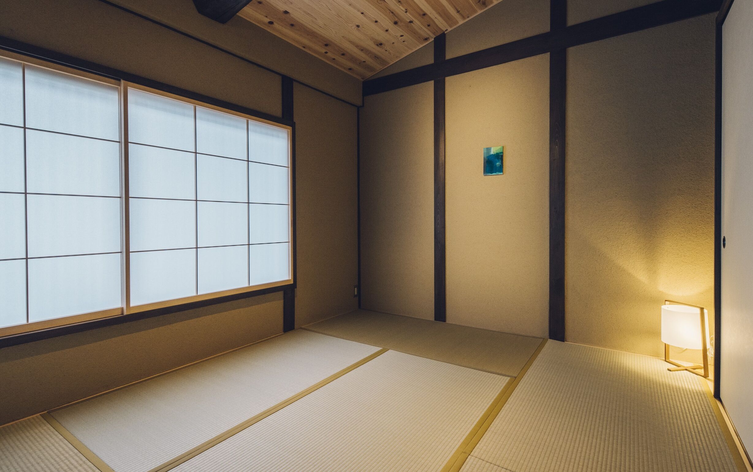 A traditional Japanese room with tatami flooring, shoji screens, and a small table with a lamp.