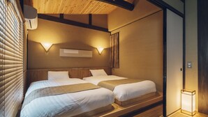 A hotel room with two beds, wooden ceiling beams, a wall-mounted air conditioner, and a bedside table with a lamp. - Someno House Kyoto Dog Friendly (Kyoto)