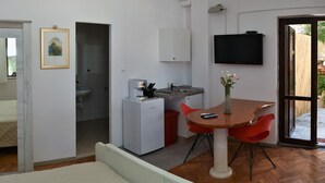 A compact living space with a kitchenette, a dining area with red chairs, a TV mounted on the wall, and a door leading to an outdoor area. - Apartment Nadja -Studio with Terrace (Supetar)