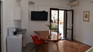 A compact kitchen with a refrigerator, a sink, and a dining table with two chairs. There is a television mounted on the wall and a door leading to an outdoor area. - Apartment Nadja -Studio with Terrace (Supetar)