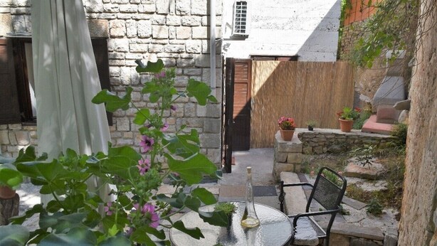 A stone building with a door, a small garden with a table and chairs, and potted plants. - Apartment Nadja -Studio with Terrace (Supetar)