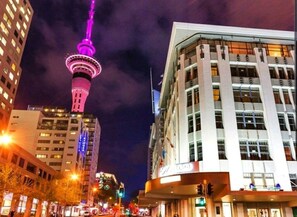 Experience the vibrant city atmosphere from the comfort of our hotel, surrounded by a striking tower and lush greenery.