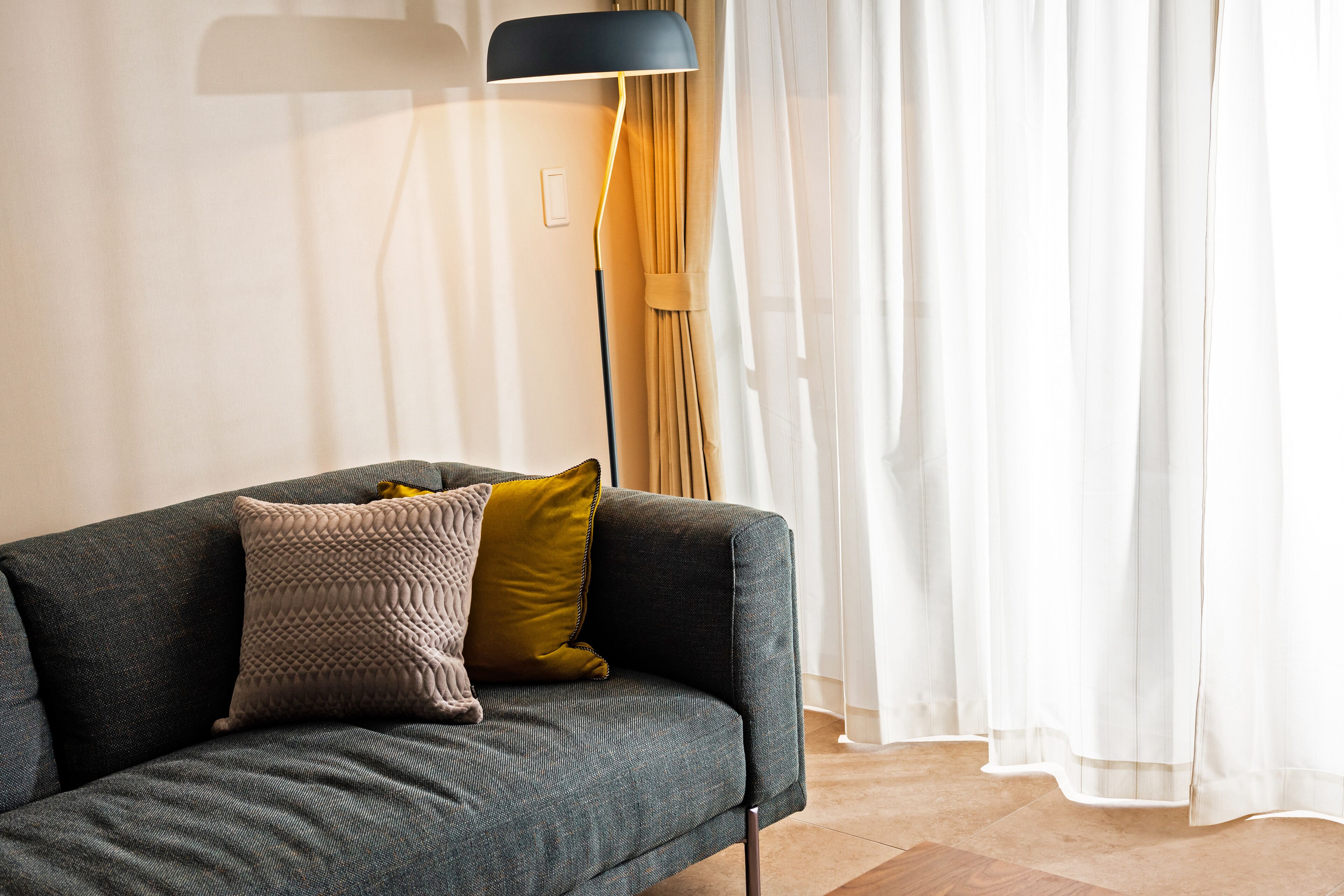 Una sala de estar moderna con un sofá gris, dos cojines, una lámpara de pie y cortinas de gasa.