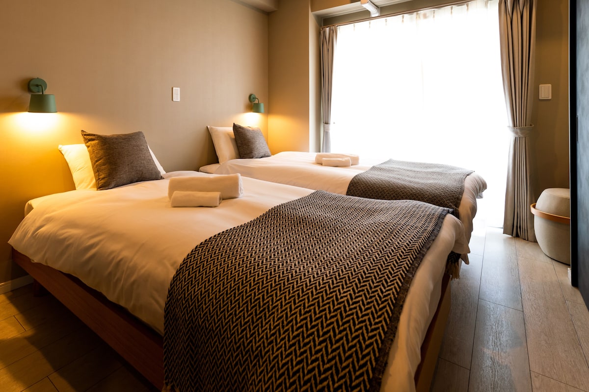 Une chambre d’hôtel avec deux lits, chacun recouvert d’un plaid à motifs, et comprenant une table de chevet et une lampe.