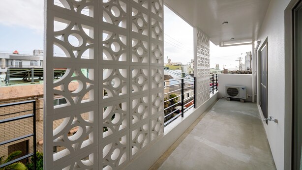 Een balkon met een witte decoratieve scheiding, een metalen hekwerk en een airconditioning.