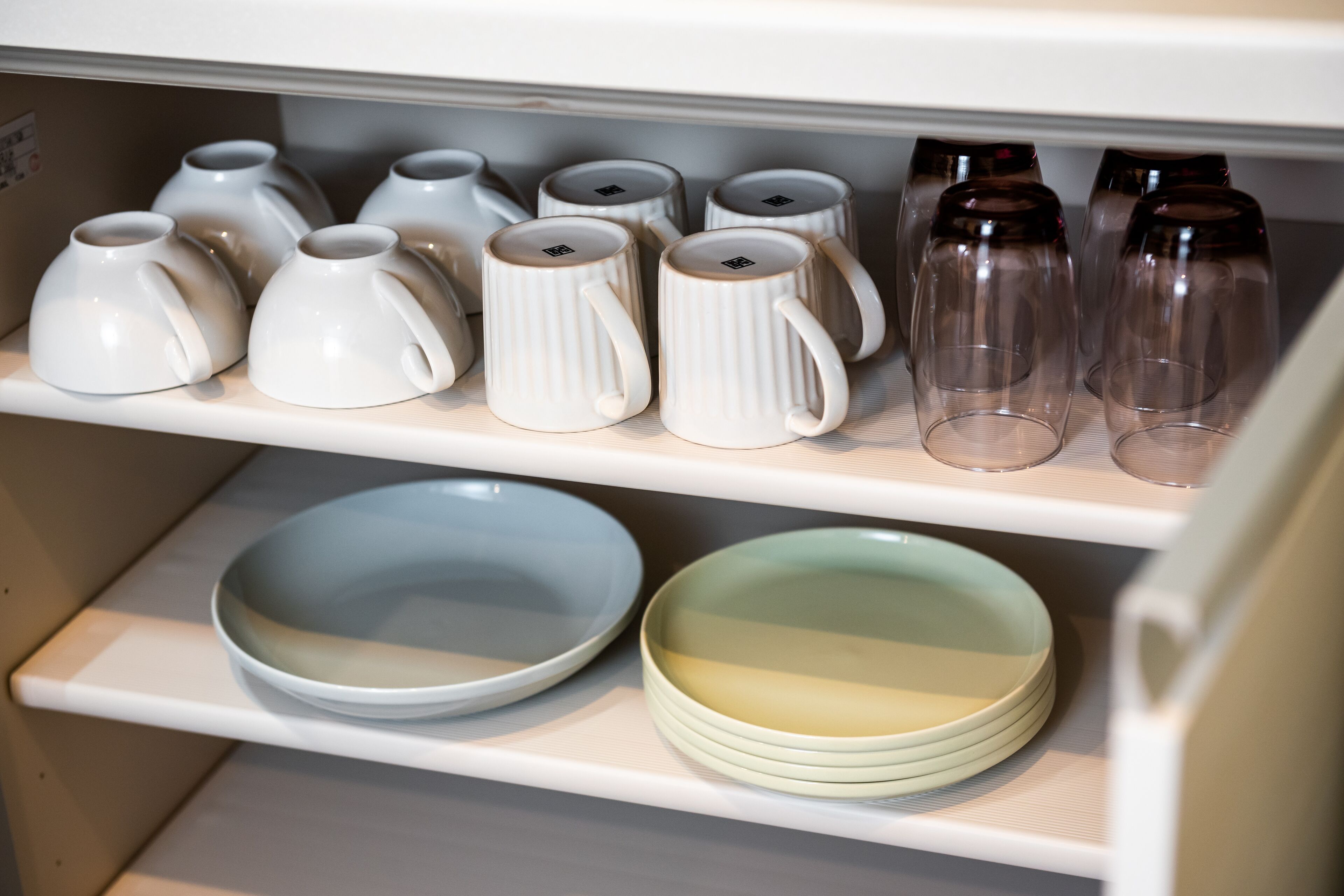 A kitchen cabinet with white mugs, clear glasses, and plates.