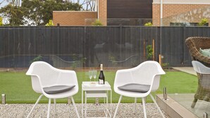 Een terras met twee witte stoelen en een tafel, een fles wijn en een glas.