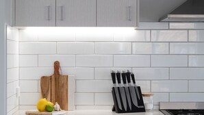Een keuken met witte tegels, een houten snijplank, een messenblok en wat citroenen en knoflook.