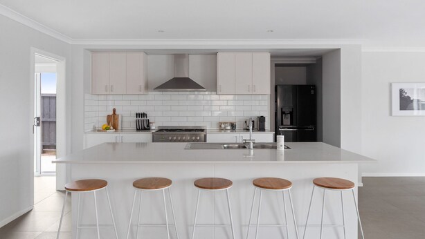 Een moderne keuken met witte kasten, een centraal kookeiland met barkrukken, een roestvrijstalen fornuis en een zwarte koelkast.