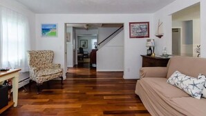 A living room with a patterned armchair, a beige sofa, wooden flooring, and a staircase leading to another room.
