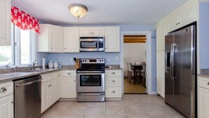 A modern kitchen with white cabinets, stainless steel appliances, and a red curtain over the window.
