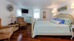 A bedroom with a bed, two chairs, a dresser, a lamp, and a painting on the wall.