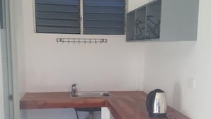 A small kitchen with a wooden countertop, a sink, a window with blinds, and a kettle on the counter. - Mystic Divers Guesthouse (San Juan)