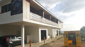 A two-story building with a balcony, a car parked in front, and a yellow bus nearby. - Mystic Divers Guesthouse (San Juan)