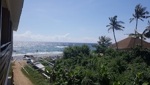 A coastal view with a beach, palm trees, and a building with a sloped roof. - Mystic Divers Guesthouse (San Juan)