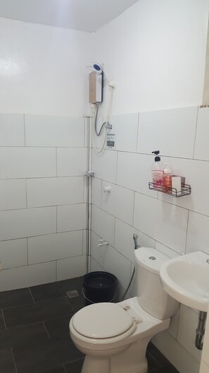 Et badeværelse med toilet, vask, bruser og en hylde med toiletartikler.